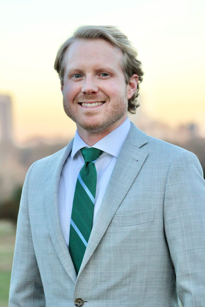 Kevin Long headshot, man in grey suit with city skyline in background